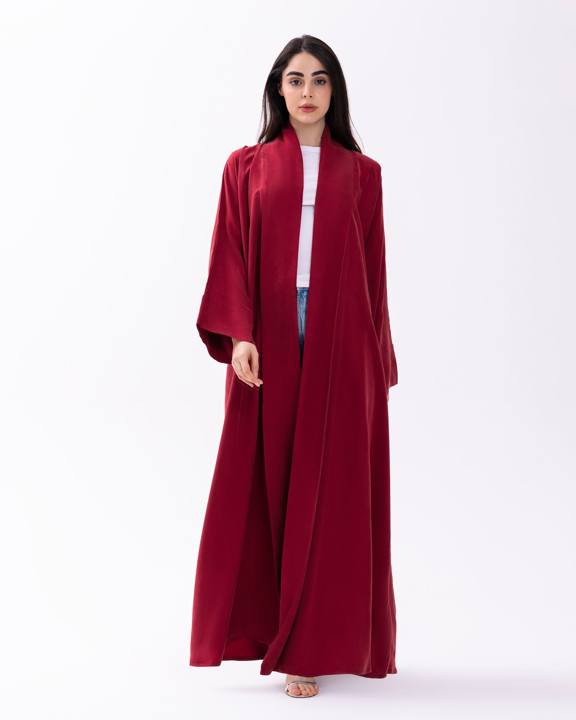Woman wearing a long burgundy abaya over a white shirt on a white background