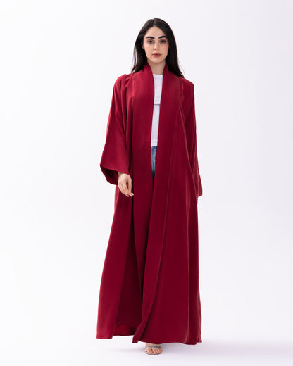 Woman wearing a long burgundy abaya over a white shirt on a white background