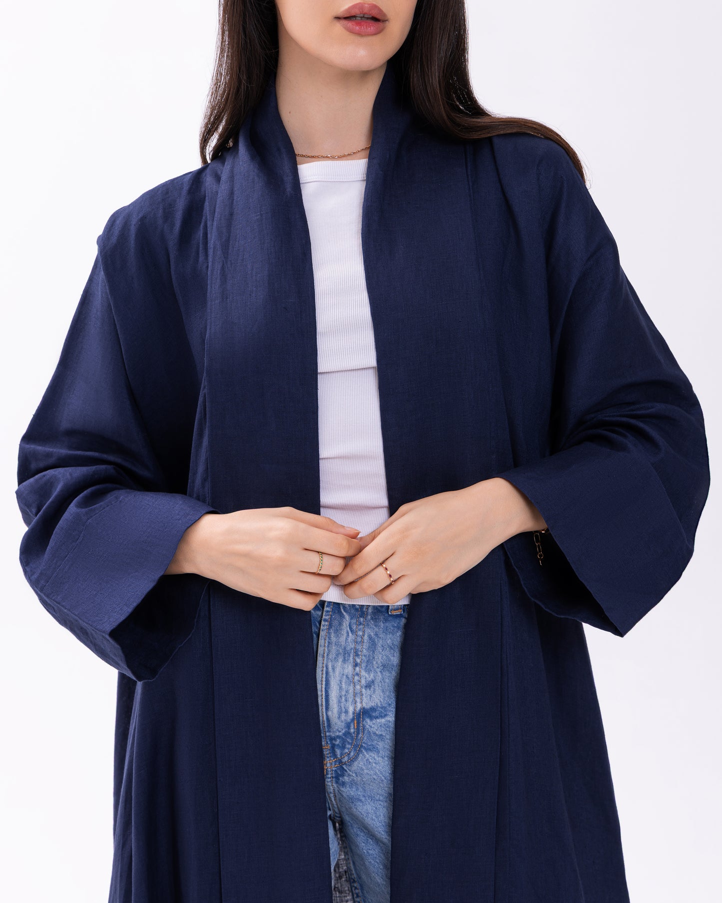 Person wearing a navy blue coat over a white top and jeans on a white background