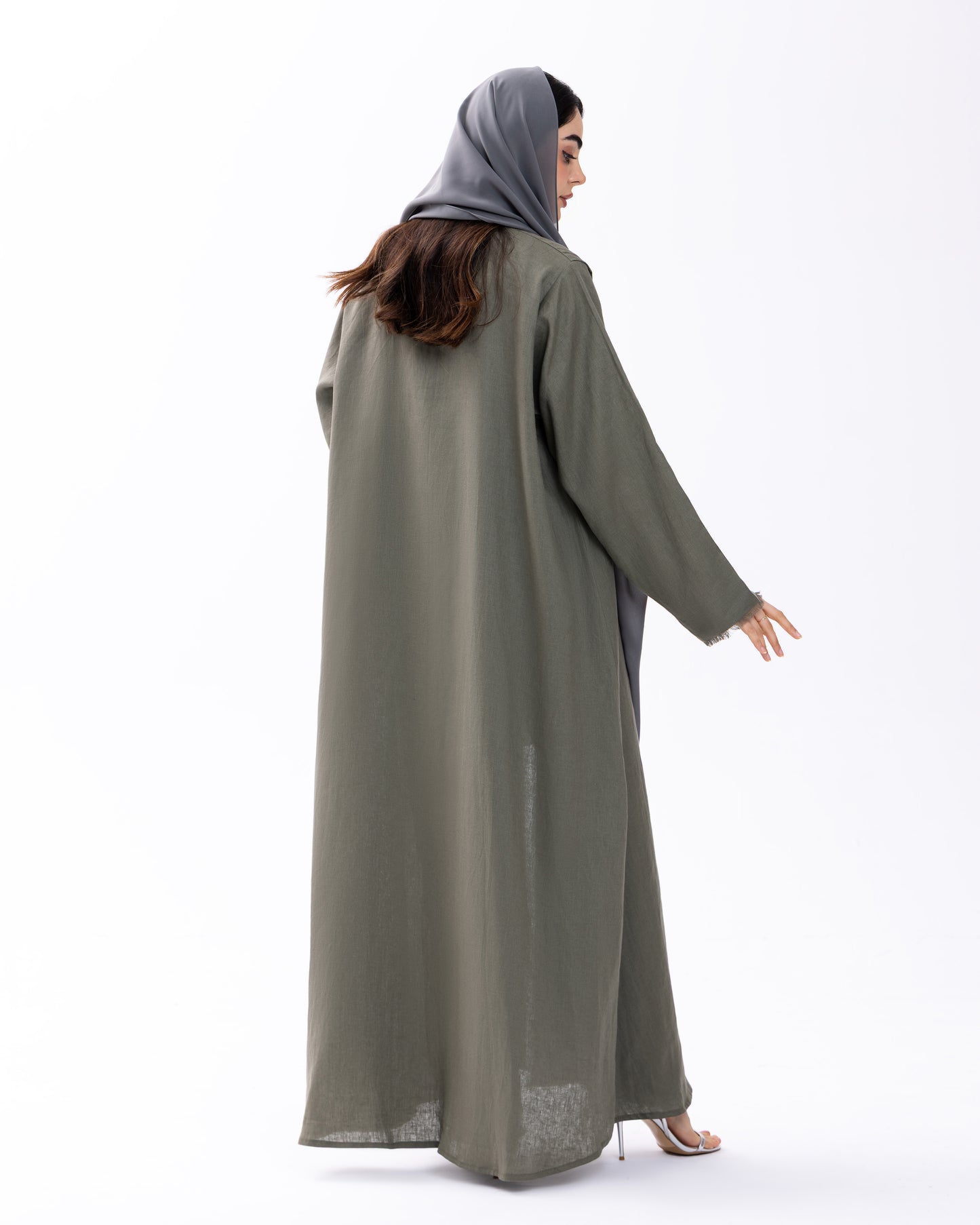 Woman wearing a long, light green abaya with a matching headscarf on a white background