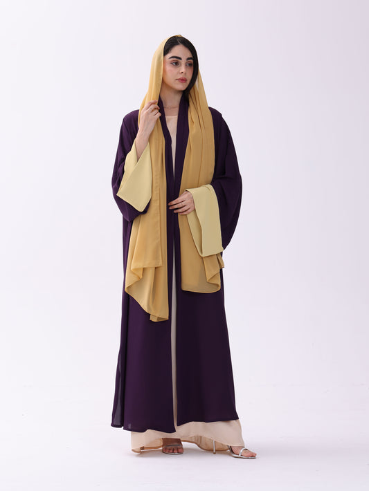 Woman wearing a long dark purple dress with a yellow hijab on a white background