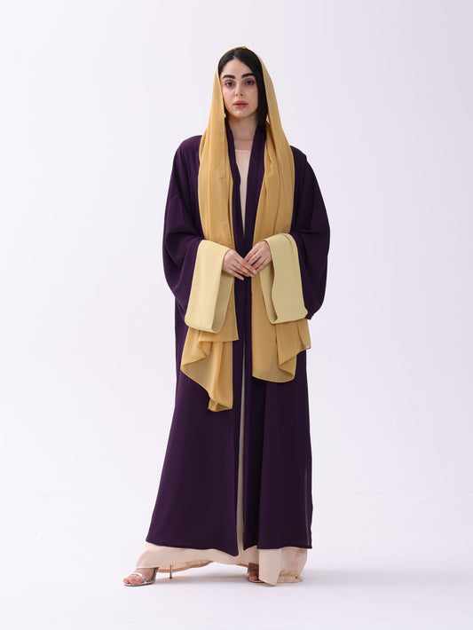 Woman wearing a dark purple abaya with a yellow scarf on a white background